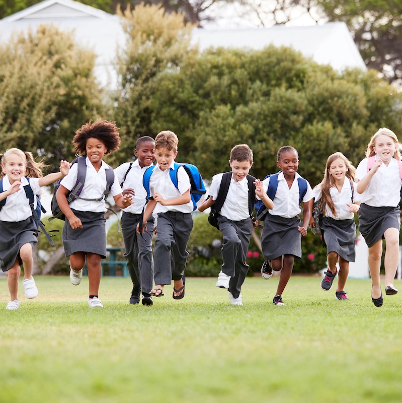 Excited Genesis school elementary school students in uniform are running in the grass