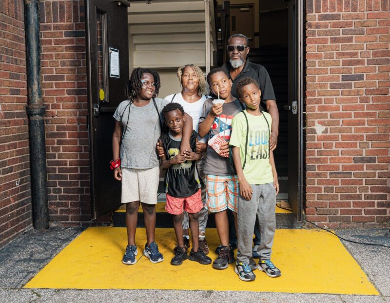 A family from The Genesis School stands together for a photo in front of the school building. 
