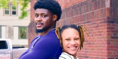 Two Genesis School teachers are standing back to back, smiling into the camera